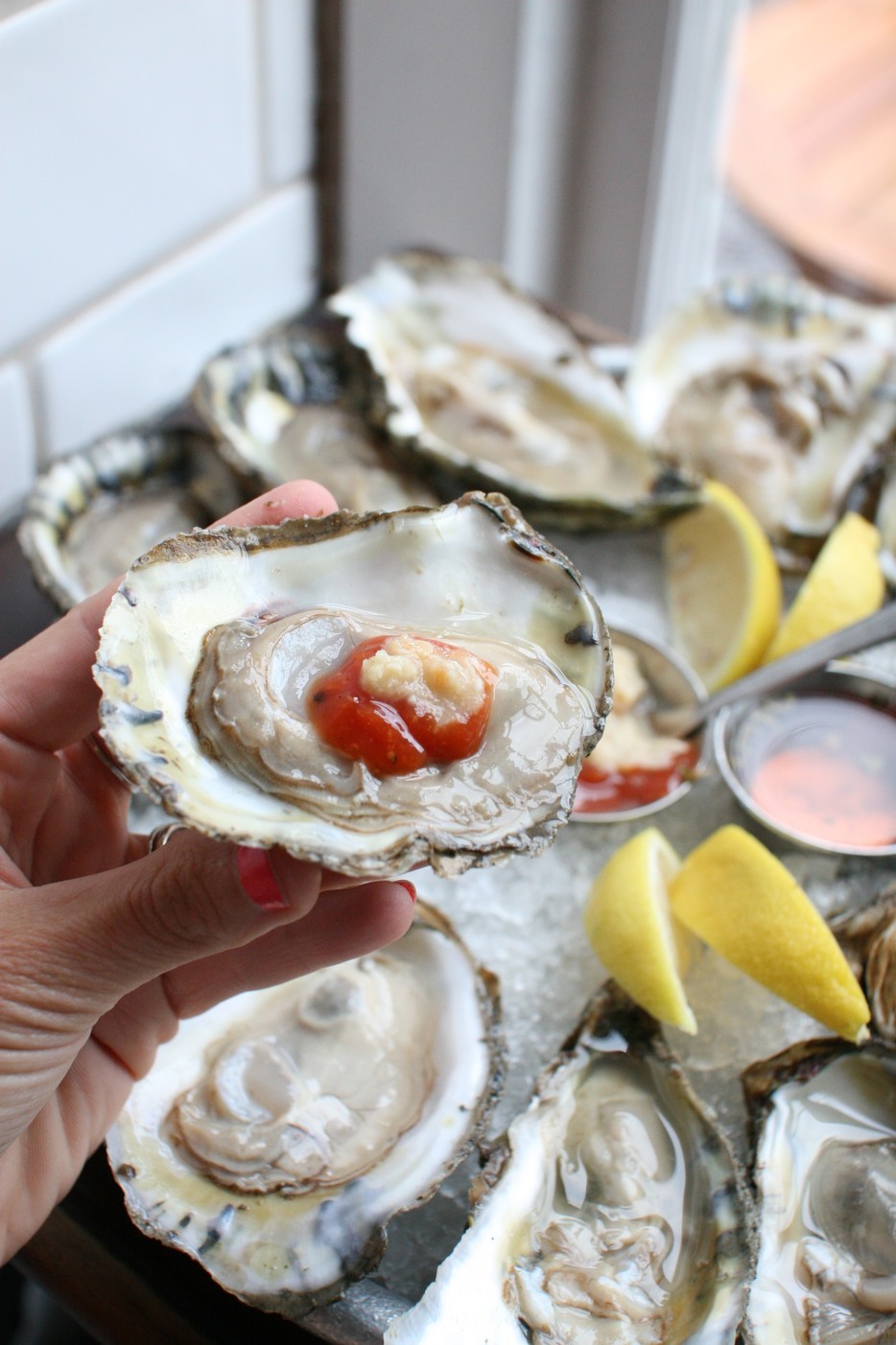 Oyster half shell with meat inside and is held above a table with other half shell oysters.